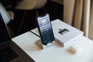 智慧型手機在支架上充電，旁邊有筆記型電腦和AirPods，放在乾淨的桌子上。 — MacBook Air 15 壁紙