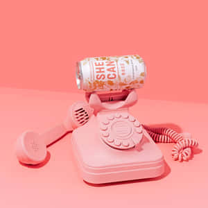 粉紅色轉盤電話機拿著一個標籤為 She Can Rosé 的粉紅色葡萄酒罐。 — 粉嫩粉彩美學 壁紙