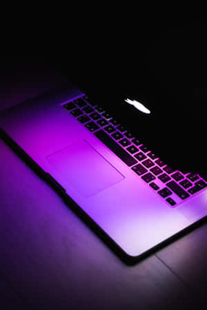 在黑暗中，木桌上發光的紫色筆記型電腦。 — 霓虹紫 壁紙