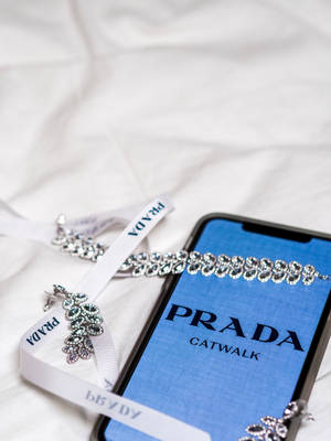 白色布料上的水晶珠寶旁邊的Prada Catwalk手機螢幕。 — 手機 壁紙