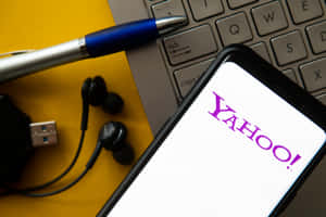 在黃色背景上，智慧型手機顯示Yahoo標誌，旁邊有筆記型電腦鍵盤和辦公室配件。 — 雅虎 壁紙