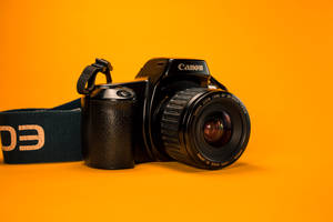 黑色Canon DSLR相機連鏡頭和肩帶，置於橙色背景上。
