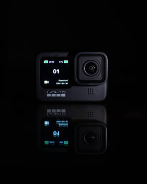 一部黑色GoPro相機在反射表面上帶有發光螢幕細節。 — 網路攝影機 壁紙