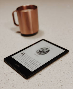 Kindle顯示書頁，旁邊有銅杯，放在有斑點的檯面上。 — Galaxy Z Fold 5 壁紙