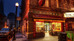 Eastern Bakery店面在黃昏時分在磚砌小巷中溫暖地發光，有街燈和停泊的貨車。 — 烘焙坊 壁紙