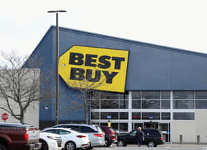 Best Buy商店外觀，有停放的汽車和一個行人走向入口。 — 購物 壁紙