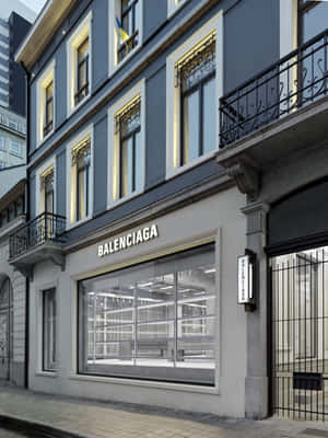 夜晚 Balenciaga 商店外觀，帶有照明窗戶和石頭建築。 — 巴黎世家 壁紙