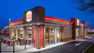 黃昏時分的Burger King速食店，帶有紅色燈光和戶外餐桌。 — 漢堡王 壁紙