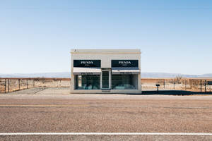 藍天下沙漠中一條路前的Prada商店。 — Prada 壁紙