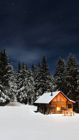 雪覆蓋的小屋，窗戶透出溫暖的燈光，位於夜晚白雪覆蓋的森林中。 — 冬季風景 壁紙