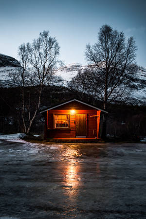 在暮色中，雪景山區裡一間溫暖照亮的木屋。 — 4K iPhone 壁紙