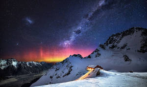 在星空和北極光下，白雪覆蓋的山上發光的小屋。 — 月亮與星星 壁紙