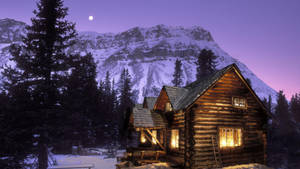 舒適的木屋，在雪地山林中亮著溫暖的燈光，暮色時分。 — 冬季風景 壁紙