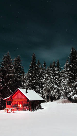 在雪地森林中，夜晚星空下，一間紅色小屋窗戶透出溫暖的光芒。 — 冬季房屋 壁紙
