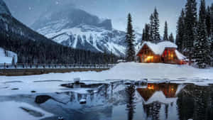 舒適小屋在雪中發光，夜間冰凍湖面反射山景 — 冬季風景 壁紙