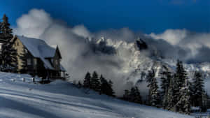 冬日山巒中隱藏著雪覆蓋的小屋，雲朵圍繞山峰旋轉。 — 白雪公主 壁紙