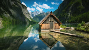 木屋漂浮在清澈的山湖上，完美倒映，背景是白雪覆蓋的山峰。 — 首頁 壁紙