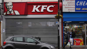 城市街道上關閉的KFC商店，帶金屬捲簾，附近有汽車和行人。 — 肯德基 壁紙