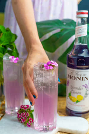 手拿著薰衣草檸檬飲料，配以粉紅花朵和Monin糖漿瓶。 — Oppo Pad 壁紙