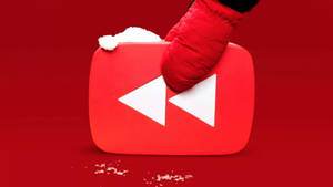 戴紅色手套的手拿著一個被雪覆蓋的YouTube播放按鈕。 — 冬季 壁紙