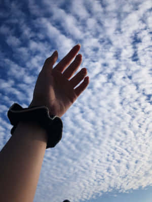 一隻手伸向有散雲的天空。 — 手牽手 壁紙