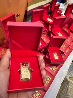 手拿著紅色盒子裡帶有兔子設計的金條，周圍有類似的盒子。 — 3:4 壁紙