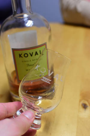 手拿著Koval威士忌品酒杯，背景有酒瓶。 — 美國 壁紙