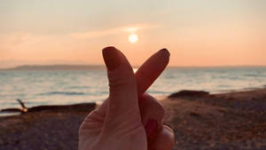 在海洋海灘日落時做出和平手勢的手 — 夕陽天空 壁紙