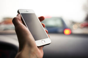 在車內手持智慧型手機，背景為模糊的交通。 — iPhone 6 壁紙