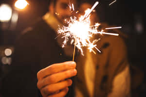 夜晚手持閃爍的煙火，背景燈光模糊。 — 慶祝 壁紙