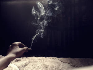 手拿著點燃的香煙，煙霧在質感白色地毯上方升起，光線昏暗。 — 抽菸 壁紙