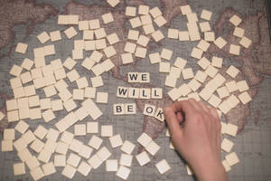 手部排列 Scrabble 字母牌，在世界地圖上拼出 'we will be ok'。 — 正向 壁紙