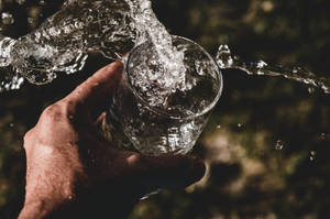 手將水倒入玻璃杯，可見水花和水滴。 — 水 壁紙