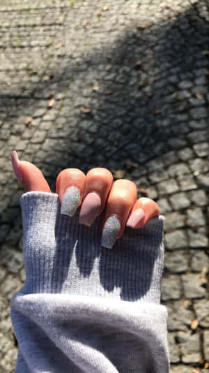 灰色袖子中的手，帶有閃粉和啞光指甲，在鵝卵石小徑上 — 指甲 壁紙