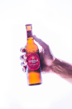 手拿著一瓶帶有冷凝水滴的冰涼Estrella Damm啤酒。 — 小米平板 8 壁紙
