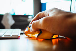 手在電腦桌上使用發光的橙色遊戲滑鼠。 — 遊戲玩家標誌 壁紙