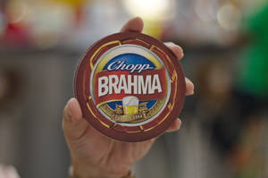 手拿著帶有標誌和小麥設計的 Brahma 啤酒杯墊。 — 品牌 壁紙