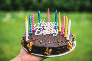 手拿著巧克力生日蛋糕，帶有蠟燭和裝飾，在戶外。 — 生日快樂蛋糕 壁紙