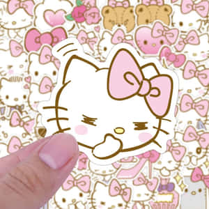 手拿著帶有粉紅色蝴蝶結的Hello Kitty貼紙，置於圖案背景上。 — 凱蒂貓 美學 GIF 壁紙