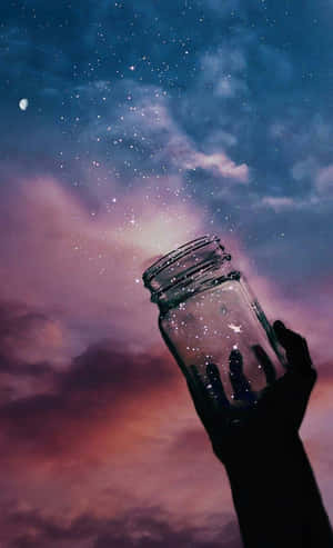 手拿著罐在帶有新月的暮色天空下捕捉流星。 — Galaxy Tab S9 FE 壁紙