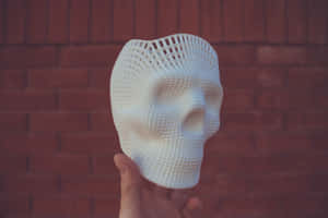 手拿著白色3D列印網格圖案頭骨，背景為紅磚牆。 — 攝影 壁紙