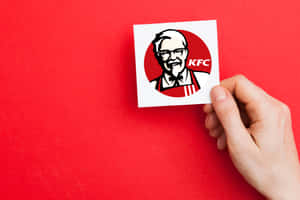 手在紅色背景上拿著KFC山德士上校標誌貼紙。 — 肯德基 壁紙