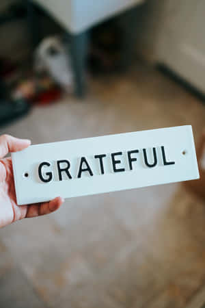 手拿著一個白色標牌，上面用黑色字母寫著grateful。 — 小米平板 9 Pro 壁紙