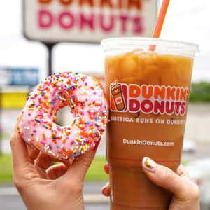 手拿著粉紅色彩針甜甜圈和Dunkin' Donuts冰咖啡。 — Dunkin Donuts 壁紙