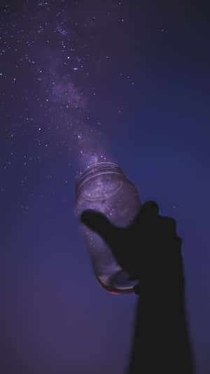 在紫色夜空下，一隻手拿著裝滿星星的罐子的剪影。 — 星星 壁紙