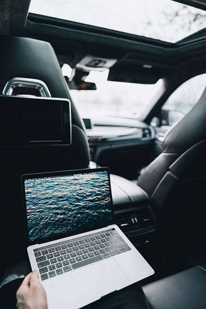 手拿著筆記型電腦，顯示海洋波浪背景，位於一輛帶天窗的黑色汽車內。 — MacBook Air 壁紙