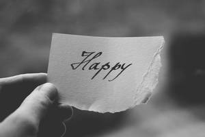 手拿撕破的紙，上面有手寫的 'Happy' 字樣，黑白配色。 — 快樂 壁紙