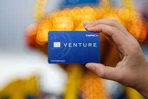 手拿著一張藍色Capital One Venture信用卡，後面有模糊的燈光。 — 金融 壁紙