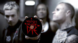 手拿著一張黑色CD，上面有紅色文字「Invaders Must Die」，前面是模糊的樂隊。 — 音樂 壁紙