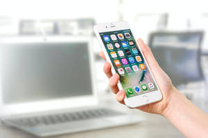 手拿著智慧型手機，在筆記型電腦前顯示應用程式。 — 插畫 iPhone 壁紙